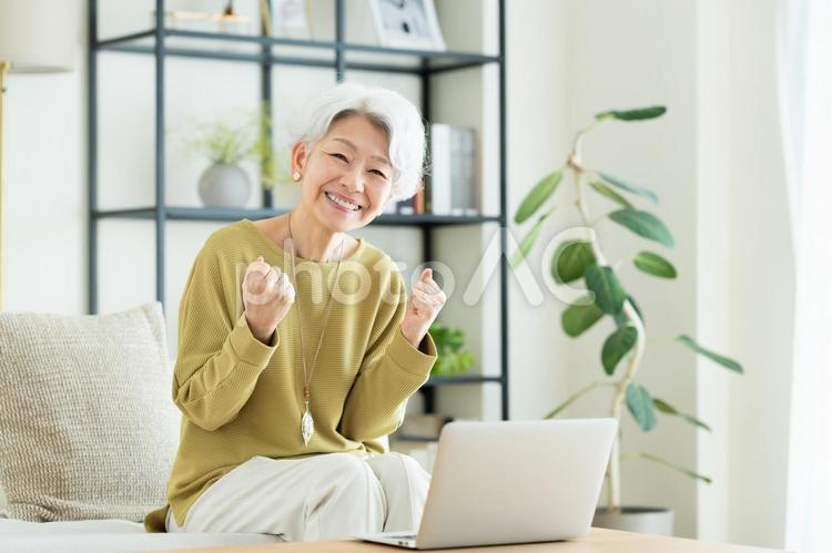 リビングでパソコンを使うシニアの女性 パソコン,ガッツポーズ,シニアの写真素材