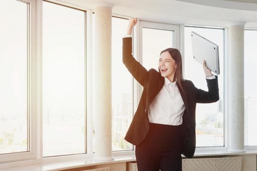 パソコンを持ちガッツポーズで外を見る女性 女性,外国人,ノートパソコンの写真素材