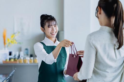 商品を渡す若い女性の店員 商品を渡す若い女性の店員の写真