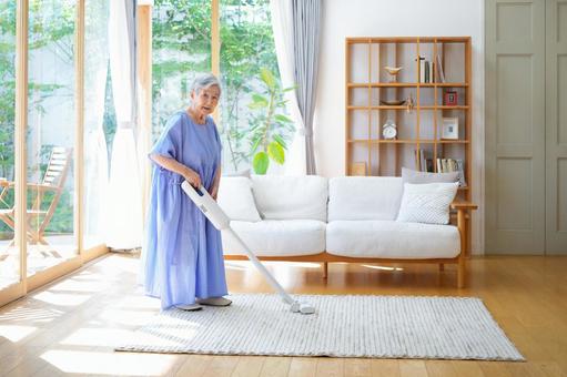 カメラ目線で掃除をする青いワンピースの女性 女性,掃除,掃除機の写真素材