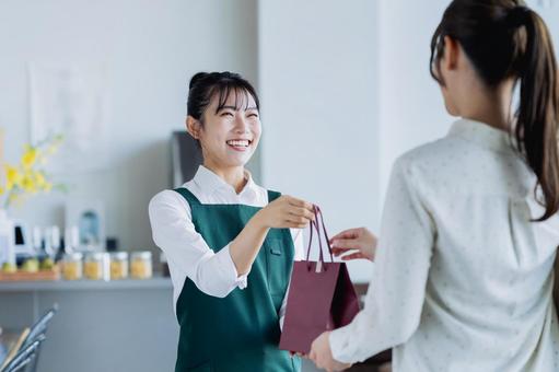 商品を渡す若い女性の店員 商品を渡す若い女性の店員の写真