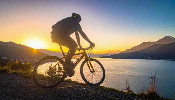 山と湖を背景にサイクリングする男性の写真