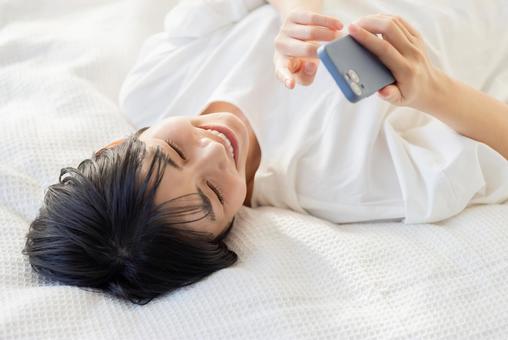 A woman lying on her back in bed and operating a smartphone, JPG A woman lying on her back in bed and operating a smartphone, JPG