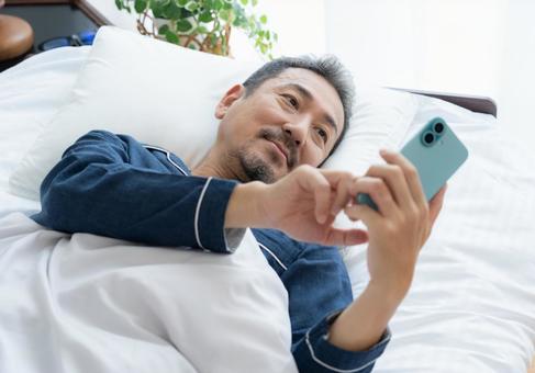 寝室でスマホを見るミドルの男性 寝室でスマホを見るミドルの男性 男性,スマホ,ミドルの写真素材