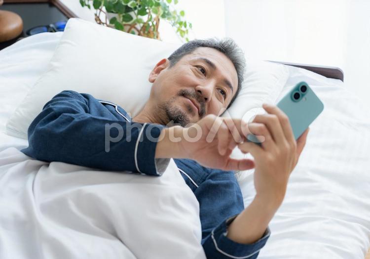 寝室でスマホを見るミドルの男性 男性,スマホ,ミドルの写真素材