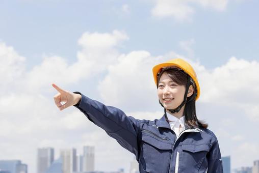 A young woman in work clothes pointing, JPG