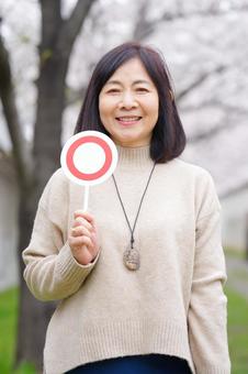 An elderly woman holding a circle sign in front of cherry blossoms, JPG An elderly woman holding a circle sign in front of cherry blossoms, JPG