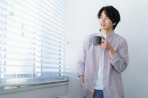 リビングの窓際でくつろぐ若い男性 男性,リビング,コーヒーの写真素材