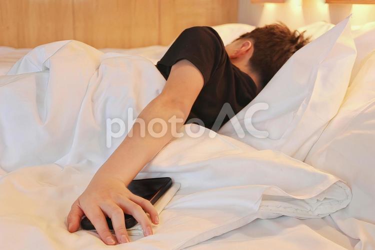 携帯電話の目覚ましを止めようとする男性 起床,朝,目覚ましの写真素材