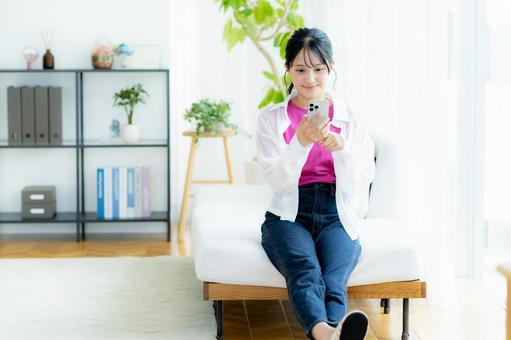部屋でスマホを操作する若い女性 スマホ,若い女性,笑顔の写真素材