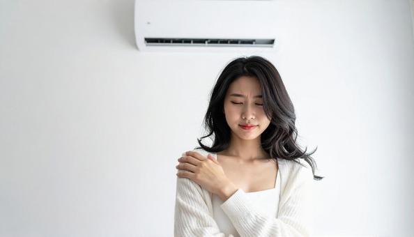 部屋のエアコンの下で寒がる女性の写真