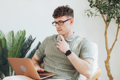 椅子に座って膝の上でノートパソコンを使う筋肉質な男性 男性,外国人,欧米人の写真素材