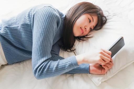 ベッドで寝る前にスマホを使う若い女性 ベッドで寝る前にスマホを使う若い女性 休み,モバイル,マンガの写真素材