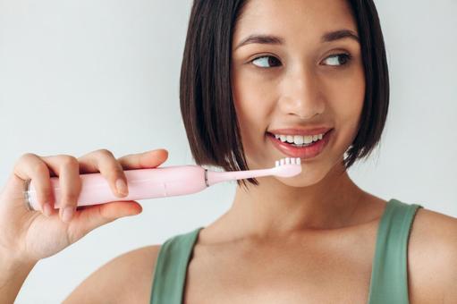 電動歯ブラシをしながら遠くを見る女性 電動歯ブラシをしながら遠くを見る女性の写真
