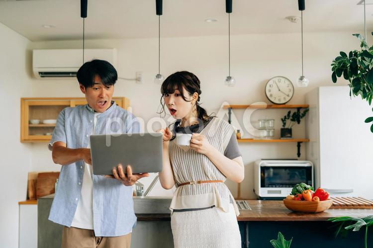 キッチンの前でパソコンを使う男女（驚く） パソコン,驚く,夫婦の写真素材