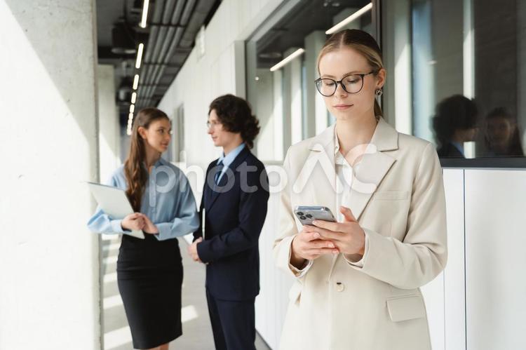 オフィスの廊下で立ち話する男女とスマートフォンを見ている女性 ビジネス,グループ,ビジネスマンの写真素材