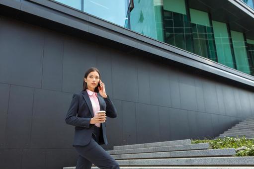オフィスビルの外の階段でコーヒー片手に電話するアジア人女性 ビジネスウーマン,ビジネス,女性の写真素材
