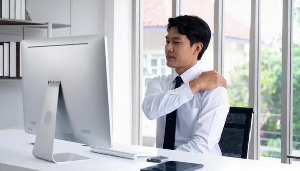 デスクワークで肩を回しほぐすビジネスマンの写真