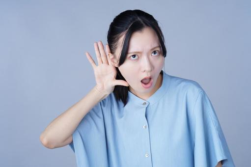 耳に手を当てる青い服の女性の写真