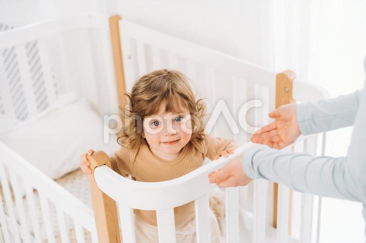 カメラ目線の笑顔の子供と抱っこしようとする手 赤ちゃん,かわいい,ベビーベッドの写真素材
