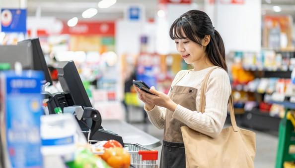 スーパーでスマホ決済を使う若い日本人女性 スーパーでスマホ決済を使う若い日本人女性の写真