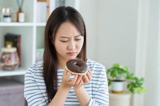 ダイエットで悩む若い女性 ダイエットで悩む若い女性 我慢,ドーナツ,ダイエットの写真素材