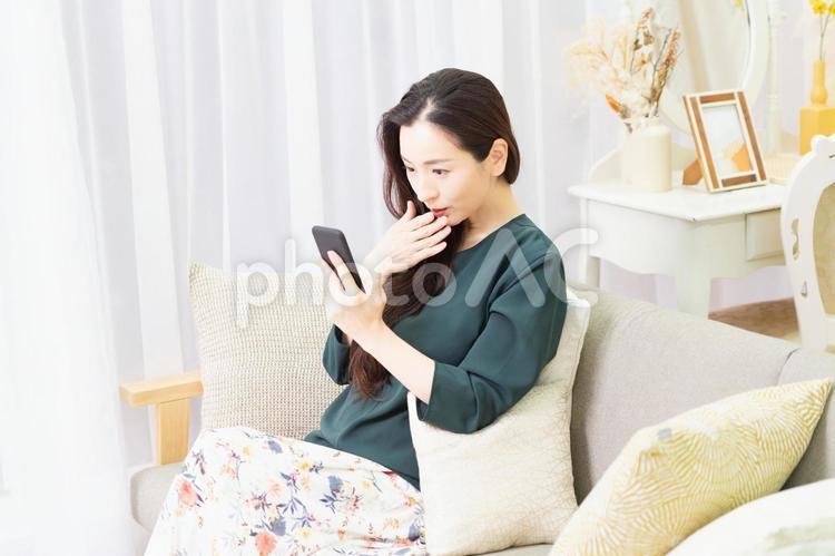 リビングのソファーに座ってスマホを操作する主婦 スマホ,ソファー,女性の写真素材