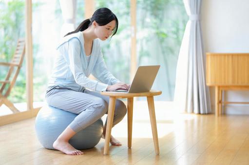 ボールに座りパソコンを見つめる女性の横顔 女性,バランスボール,ノートパソコンの写真素材