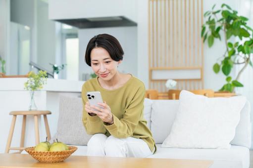 リビングでスマホを使うミドルの女性 リビングでスマホを使うミドルの女性の写真