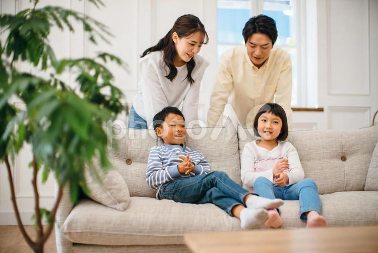 ソファで寛ぐ姉弟の背後に立つ親 親子,ファミリー,子供の写真素材