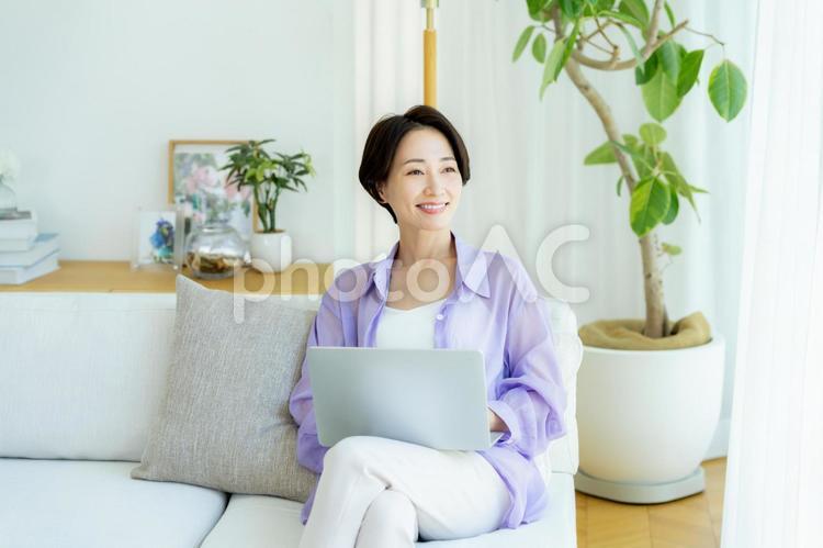 部屋でノートパソコンを使うミドル女性 女性,笑顔,テーブルの写真素材