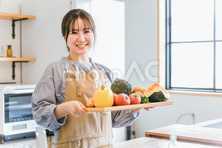 野菜を持ってキッチン立つエプロン姿の女性 野菜,主婦,料理の写真素材