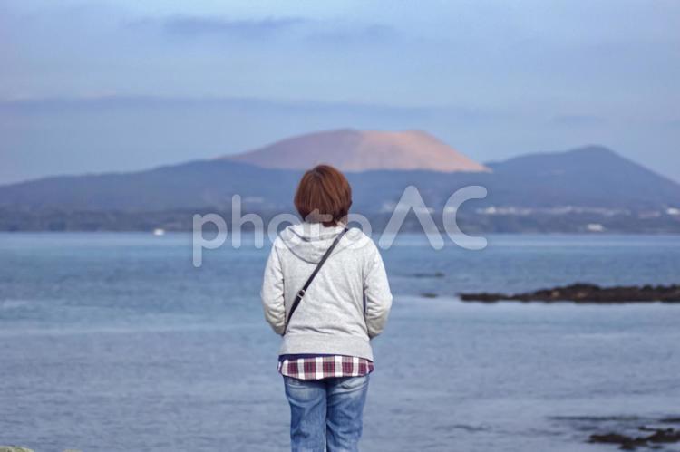 ＜人物＞海辺で鬼岳を見詰める女性の後ろ姿 女性,悩む,空の写真素材