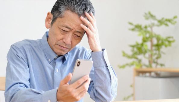 スマホの画面を見て困惑する高齢の男性 スマホの画面を見て困惑する高齢の男性の写真