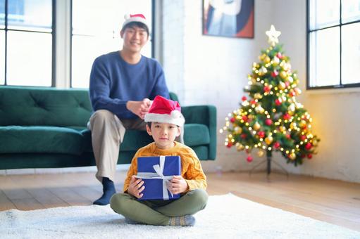 プレゼントを持ってあぐらの男の子と後ろで座る男性 プレゼントを持ってあぐらの男の子と後ろで座る男性の写真