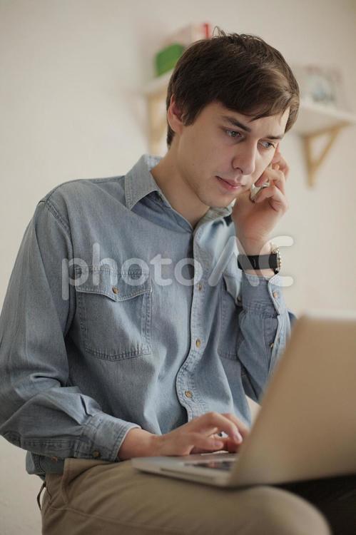 電話しながらＰＣを操作する外国人青年2 男性,青年,電話の写真素材