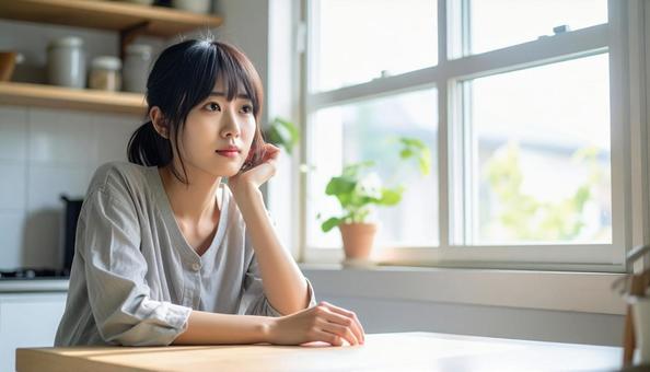 疲れた表情でキッチンに座る若い女性 疲れた表情でキッチンに座る若い女性の写真