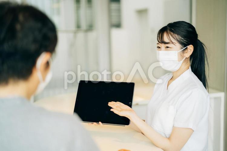 病院の受付にいる女性（マスク・患者・タブレットPC） 医療事務,電子カルテ,タブレットpcの写真素材