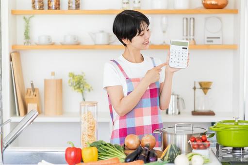 キッチンで電卓を持つ主婦。 キッチンで電卓を持つ主婦。の写真