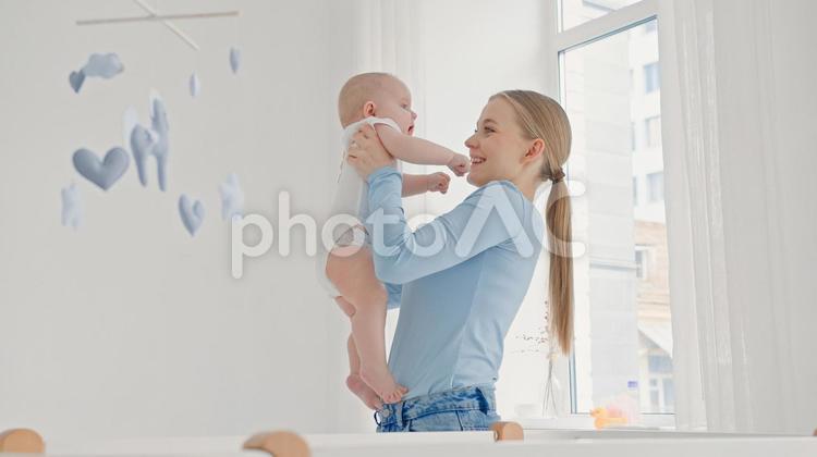 窓際で赤ちゃんを抱き笑う長袖の女性 親子,抱っこ,赤ちゃんの写真素材