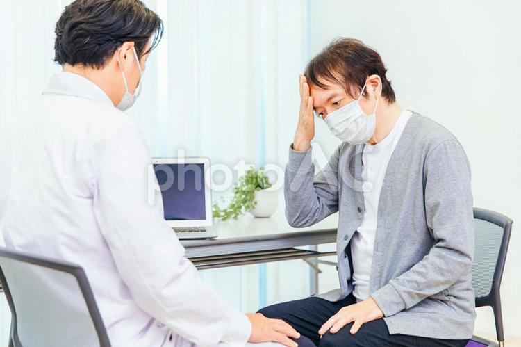 パソコンで診察するマスク姿の男性医師（頭痛） 認知症,痴呆症,脳ドックの写真素材