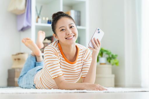 リビングでスマホを使う若い女性 リビングでスマホを使う若い女性の写真