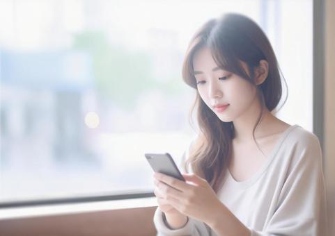カフェの窓際でスマホを見る女性のイメージ カフェの窓際でスマホを見る女性のイメージの写真