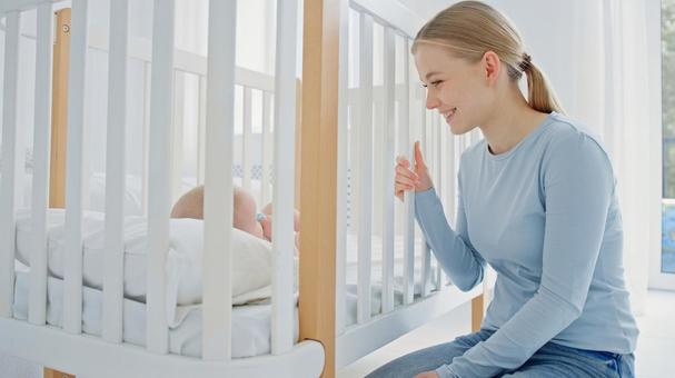 ベビーベッドの中の赤ちゃんを見て笑う女性 ベビーベッドの中の赤ちゃんを見て笑う女性 女性,ベビーベッド,見るの写真素材