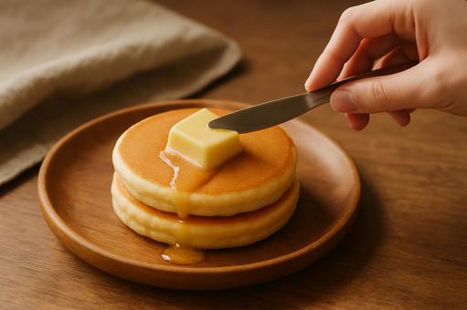 バターをホットケーキにのせる手元 バターをホットケーキにのせる手元の写真