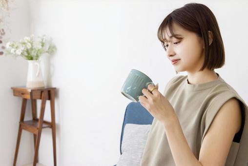 ソファーに座ってコーヒーを飲む女性 ソファーに座ってコーヒーを飲む女性の写真