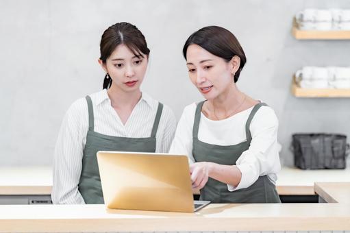 パソコンを見るエプロンをつけた女性 パソコンを見るエプロンをつけた女性 pc,パソコン,二人の写真素材