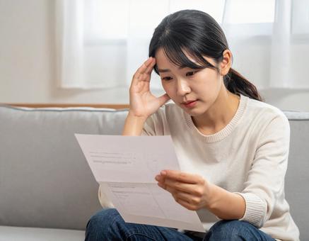 請求書を見て悩んでいる女性 請求書を見て悩んでいる女性の写真