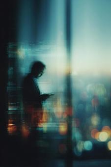 夜景を見ながらタブレットを使う男性 夜景を見ながらタブレットを使う男性の写真