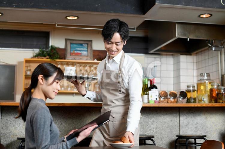 飲食店で女性客に食事の配膳をする男性店員 飲食店,レストラン,カフェの写真素材